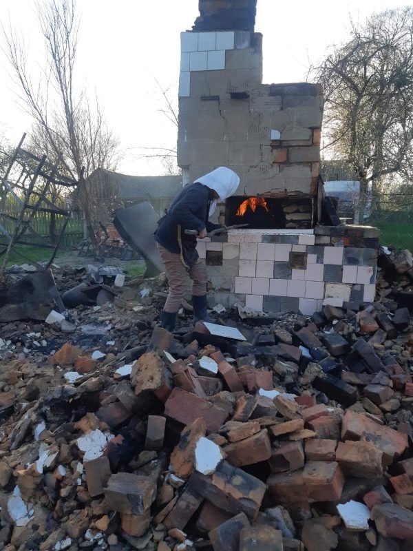 У печі, яка стоїтьна руїнах будинку,  жінка готує їжу 